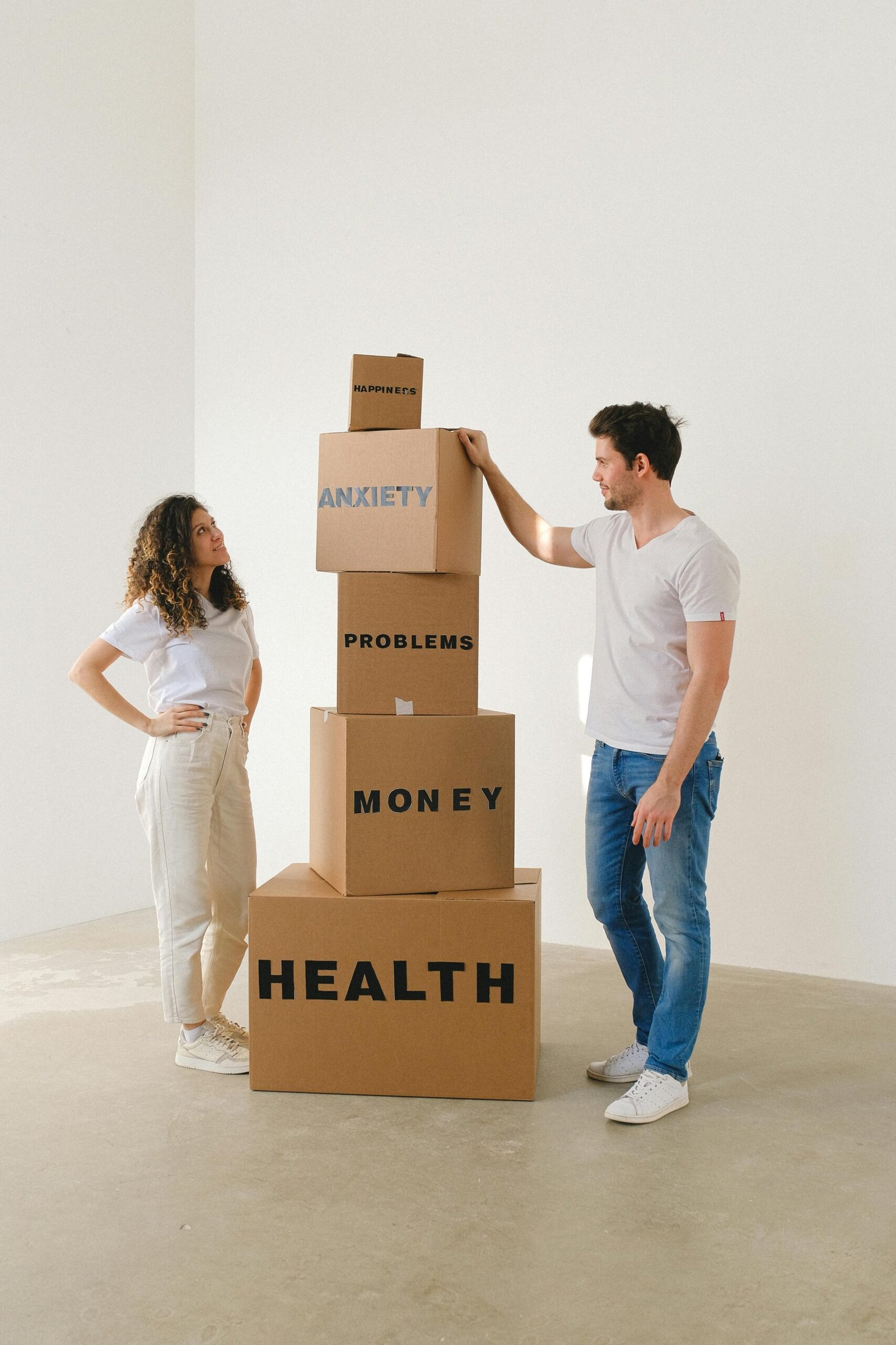 A man and woman standing beside stacked boxes labeled with stress-related words in a bright room.